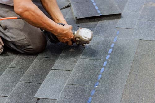 team member installing shingles on roof